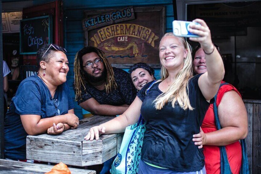 A group of people taking a selfie in front of a restaurant with a sign that reads 'Killer Grub Fisherman's Cafe.' 1