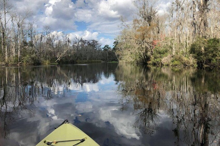 A calm river with a green kayak, trees reflecting on the water, and a partly cloudy sky. 4