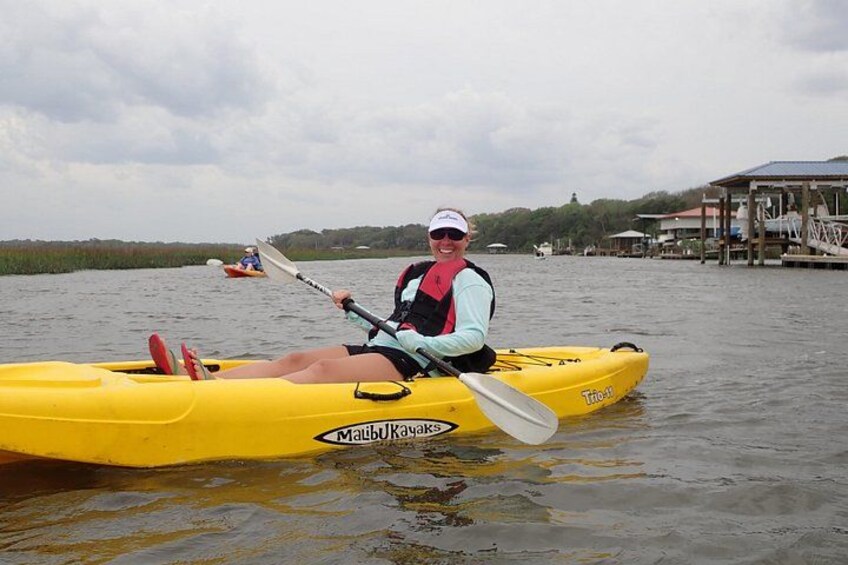 A person kayaking on a calm body of water with a dock and buildings in the background. 2