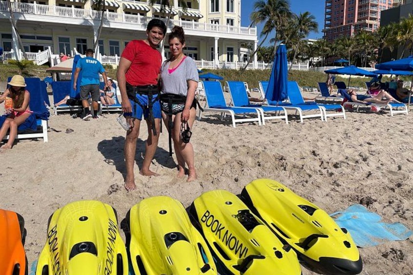 Una playa con motos acuáticas amarillas, gente y un edificio al fondo. 4