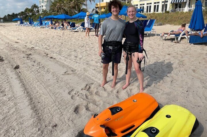 To personer står på en sandstrand med surfboards og en jetski i forgrunden. 5