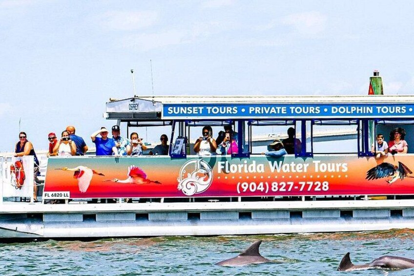 A boat with people on board, a dolphin in the water, and a banner advertising Florida Water Tours. 2