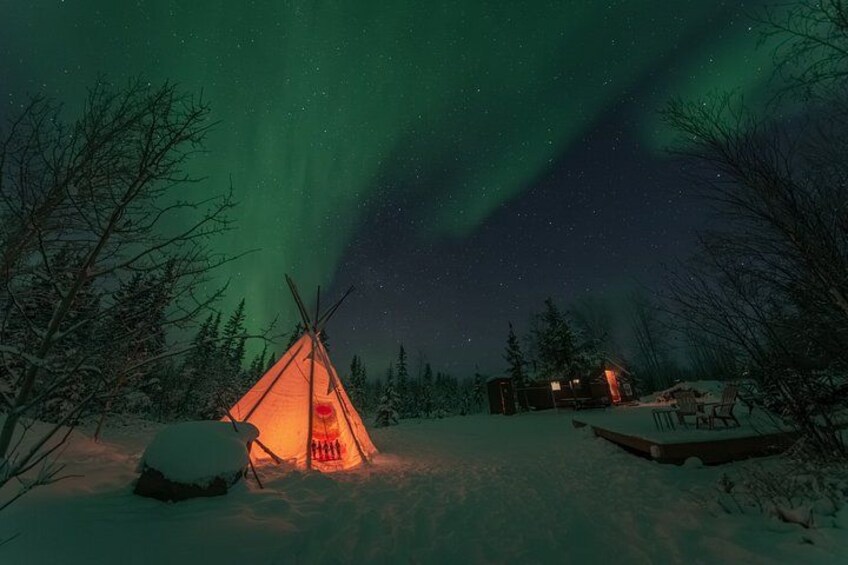 Un paysage enneigé, avec une yourte illuminée et une cabane, le tout sous un ciel illuminé par des aurores boréales. 1