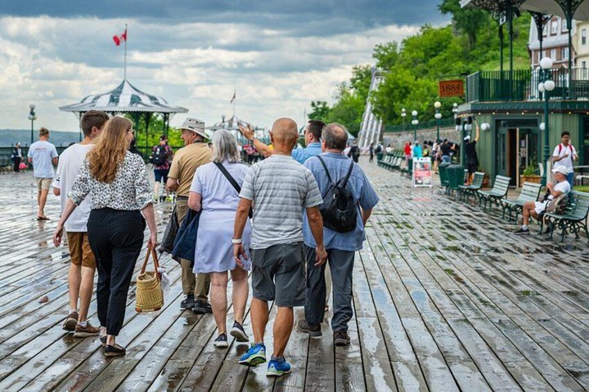 Una passerella in legno con persone che passeggiano, un gazebo e un edificio con un cartello. 1