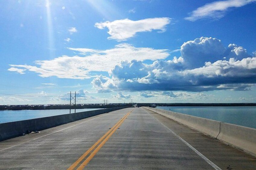 A bridge with a concrete barrier, a yellow line, and a clear sky with clouds. 4