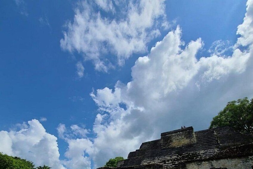 A clear blue sky with scattered clouds, ancient stone ruins, and lush green foliage. 3