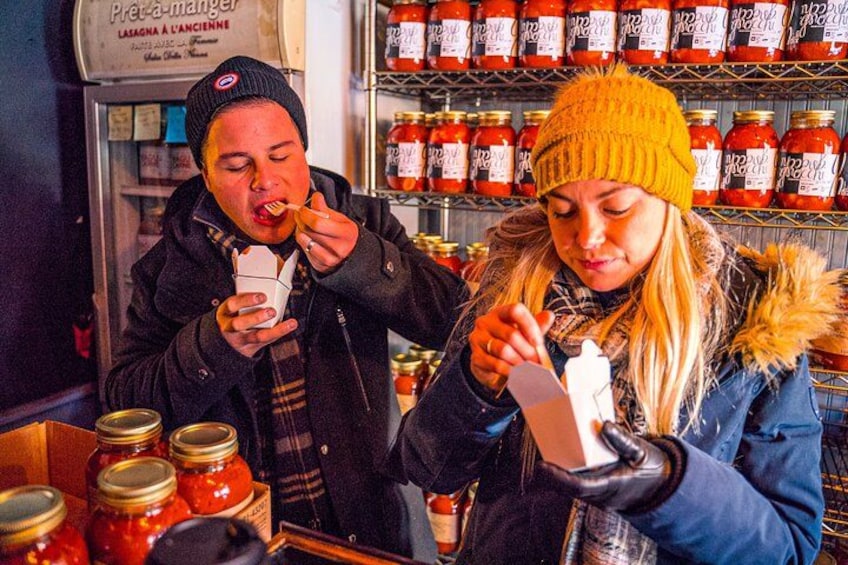 Two people tasting food at a food stall with jars of sauces in the background. 4