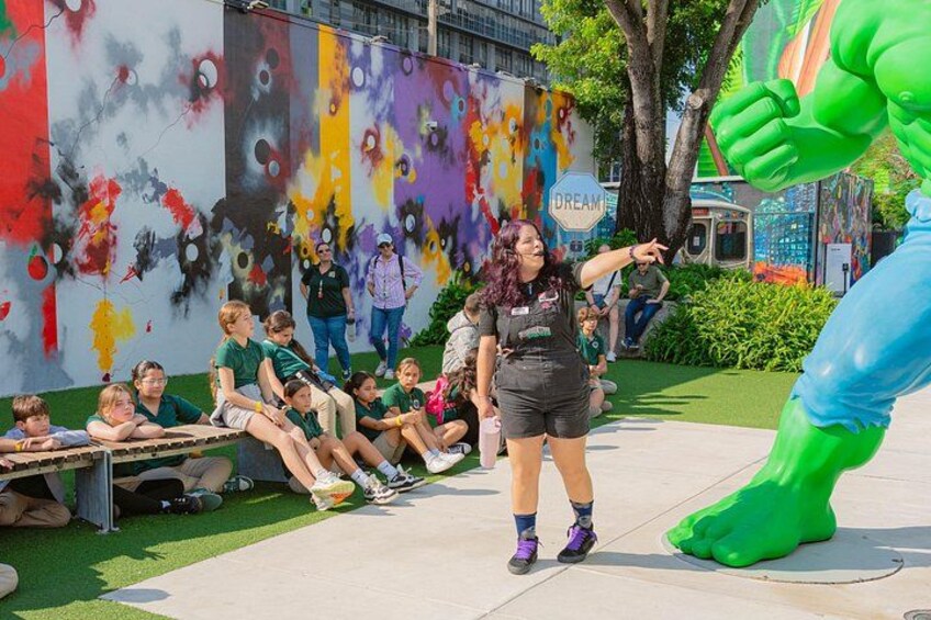 Eine Person in einem grünen Kostüm interagiert mit Kindern und einer großen grünen Statue. 4