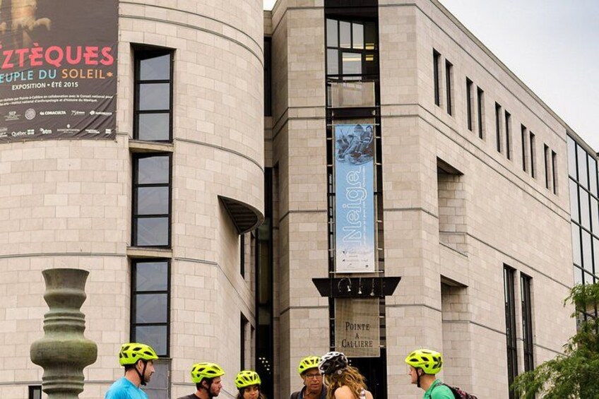 Ein Gebäude mit einer gewölbten Fassade, einem großen Banner und einer Gruppe Radfahrer mit Helmen. 2