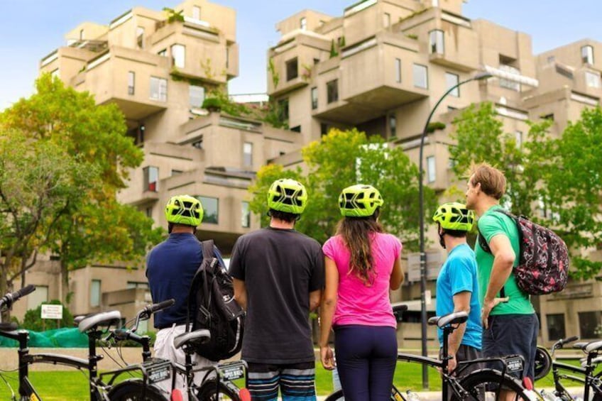 A group of people with bicycles and helmets, standing in front of a building with balconies. 1
