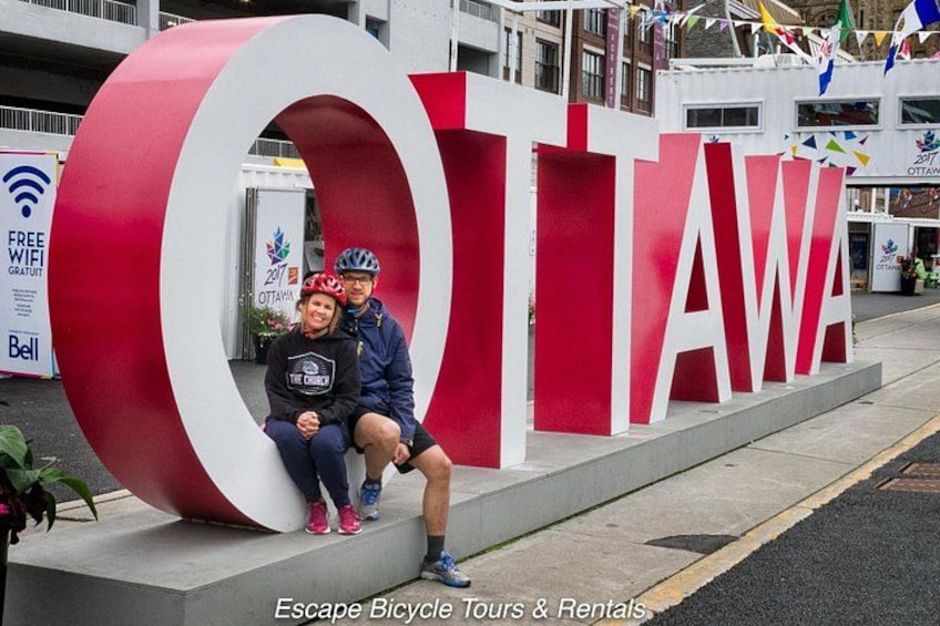 Ein großes, rot-weißes Schild mit der Aufschrift 'OTTAWA', darin sitzen zwei Personen. 2