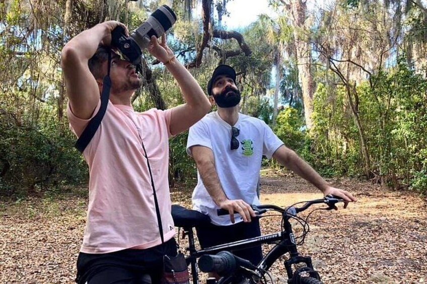 Two people, one with a camera and another on a bicycle, in a wooded area. 5