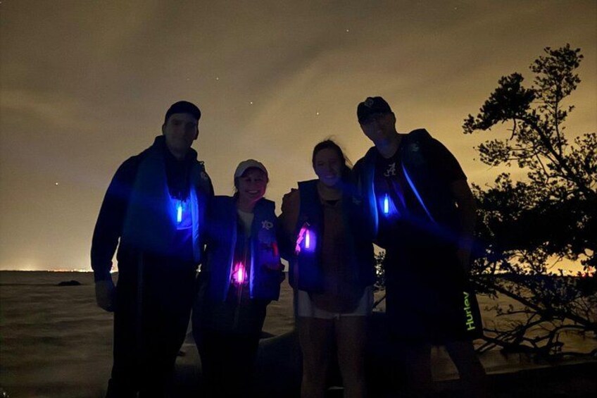 Four people standing outdoors at night with glow sticks. 2