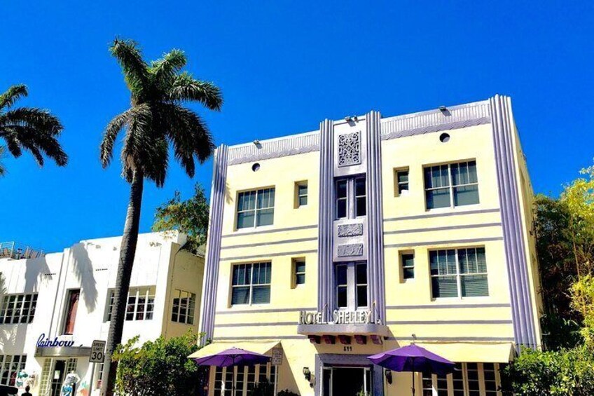 A hotel with a yellow facade, purple accents, and palm trees in the background. 2