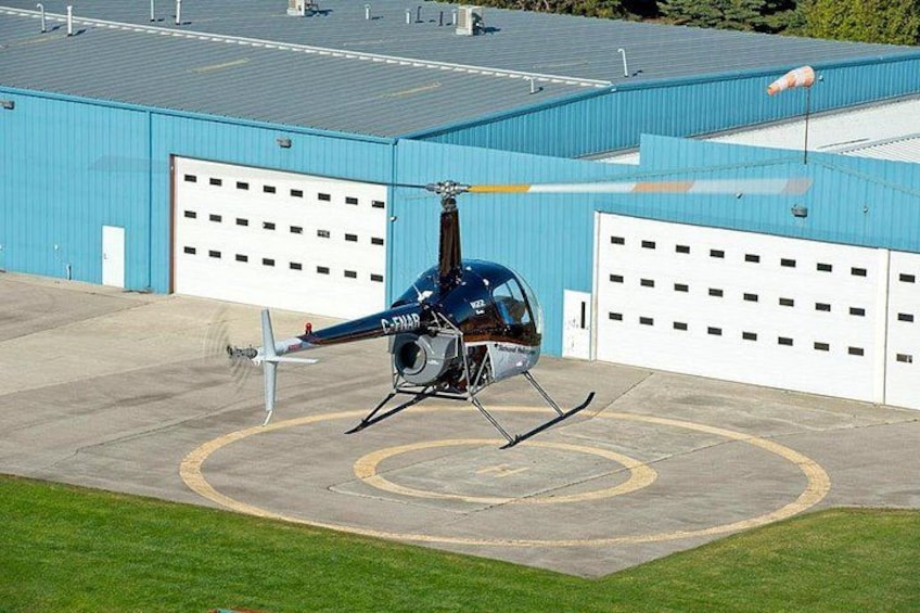 Un helicóptero en una plataforma de aterrizaje con un edificio azul y puertas de garaje blancas al fondo. 2