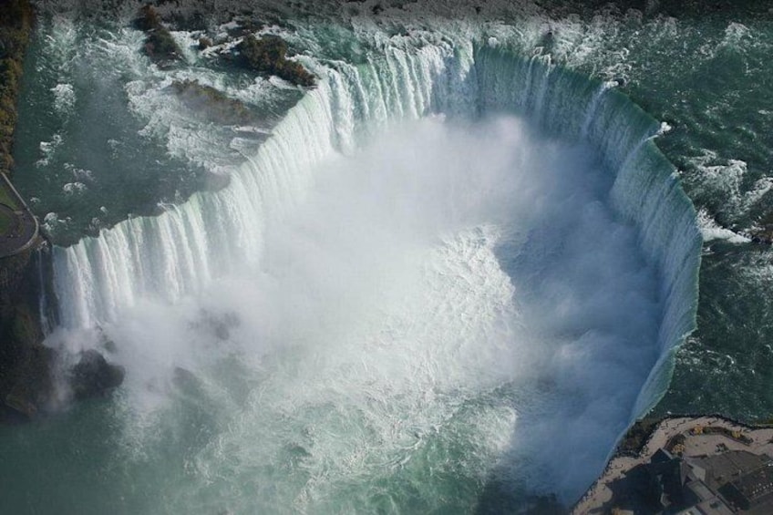 Una cascada grande con una bruma al pie, rodeada de terreno rocoso y un pequeño asentamiento. 3