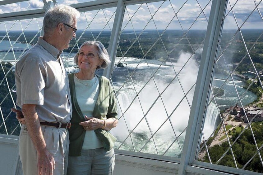 Two people standing by a large window overlooking a waterfall. 2