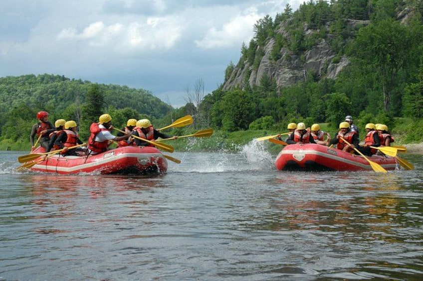 Zwei rote Schlauchboote mit Menschen, die auf einem von Grünflächen gesäumten Fluss rudern. 5