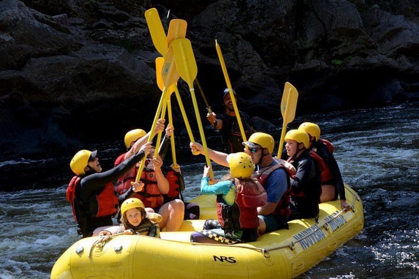 Eine Gruppe von Menschen in einem gelben Luftboot auf einem Fluss, mit Helmen und Schwimmwesten. 4
