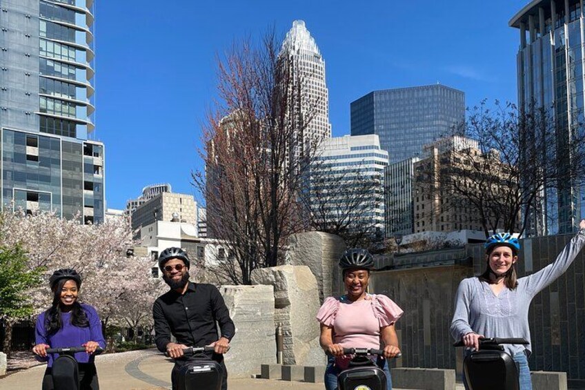 Four people on bicycles in an urban setting with modern buildings and cherry blossoms in the background. 1