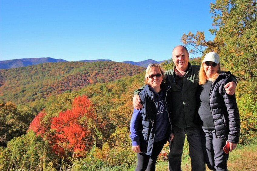 A family of three standing on a hill with autumn foliage and a mountain range in the background. 4