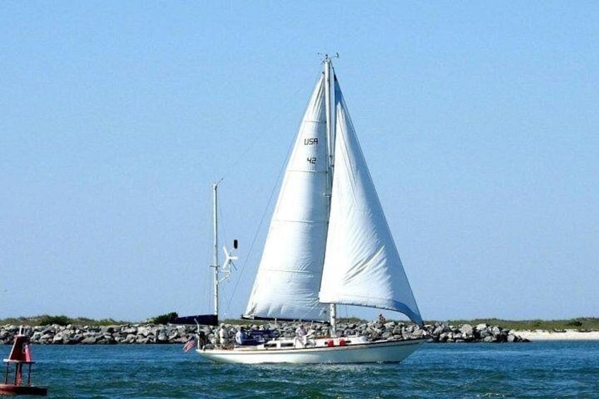 A sailboat with a white sail on calm water, surrounded by rocks and a clear sky. 1