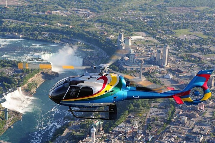 En färgglad helikopter flyger över en kuststad med ett vattenfall och industriella byggnader. 2