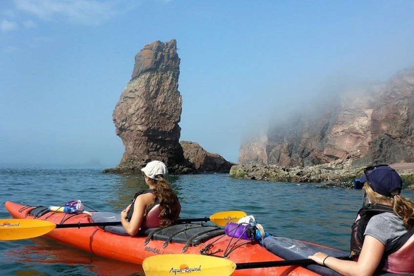 Dos personas remando en kayak en un mar tranquilo, con una gran formación rocosa al fondo. 2