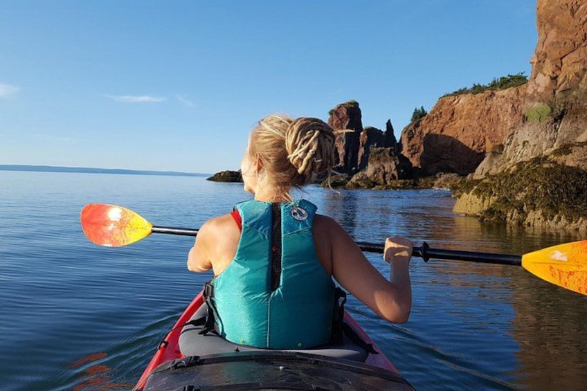 Una persona en kayak sobre aguas tranquilas, con una costa rocosa al fondo. 4