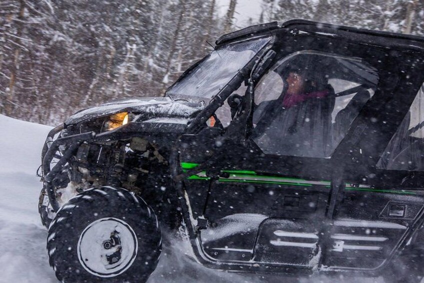 Un véhicule recouvert de neige, avec une personne à l’intérieur, qui roule à travers un paysage enneigé. 3