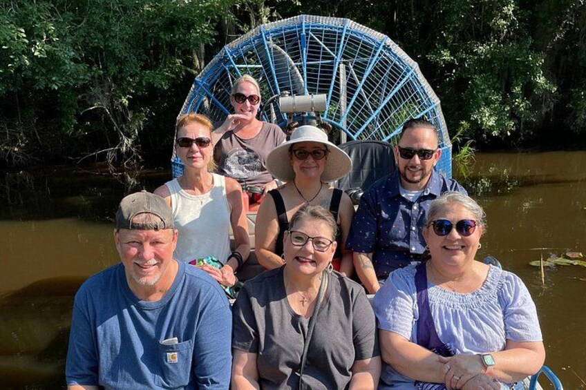 A group of people on a boat with a blue canopy, surrounded by water and greenery. 3
