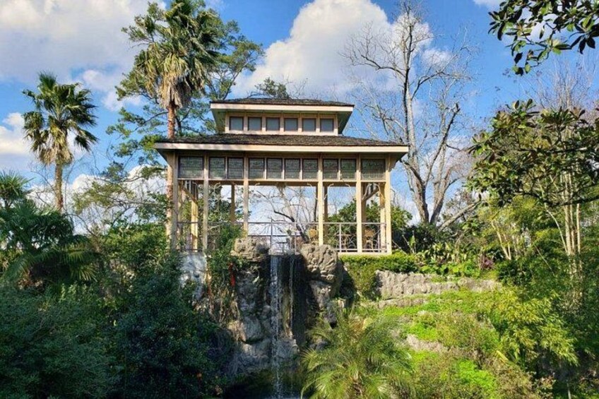 A pavilion with a stone base, surrounded by lush greenery and palm trees. 5