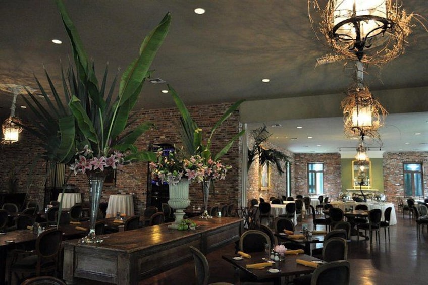 A restaurant interior with brick walls, large potted plants, and a chandelier. 2