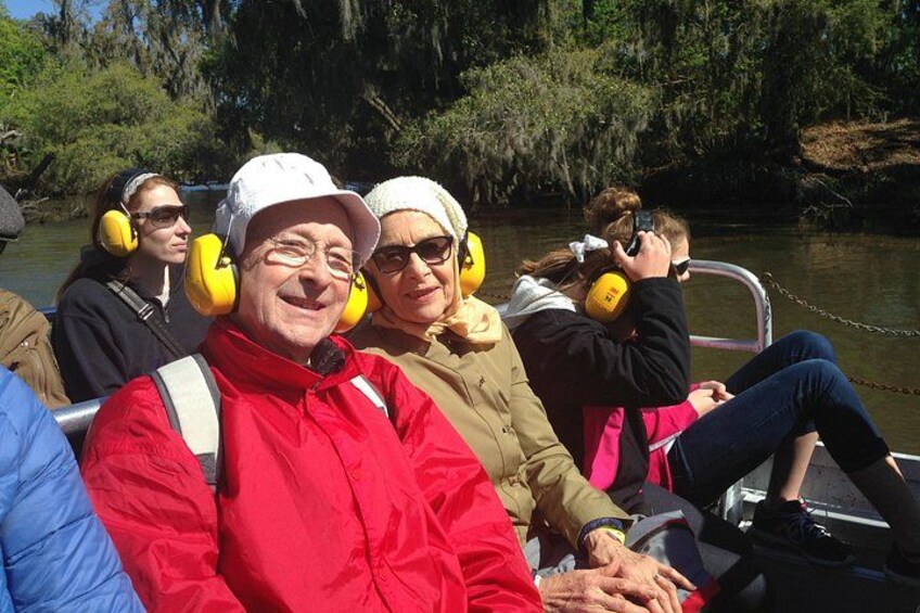 People on a boat with yellow ear protection, a river, and trees in the background. 4