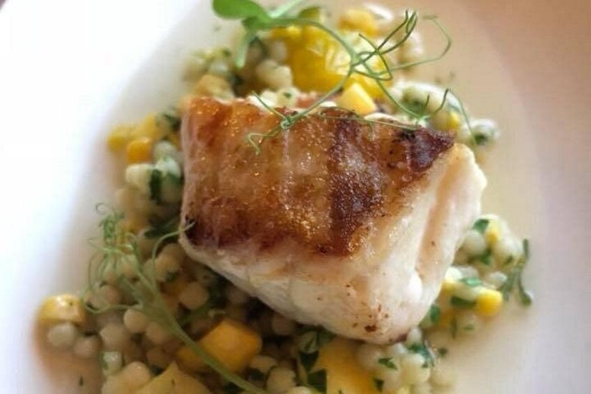 Un trozo de pescado a la parrilla en un plato, acompañado de maíz y verduras verdes. 2