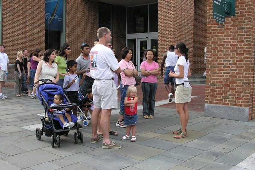 A group of people standing on a sidewalk in front of a building with a brick facade. 4