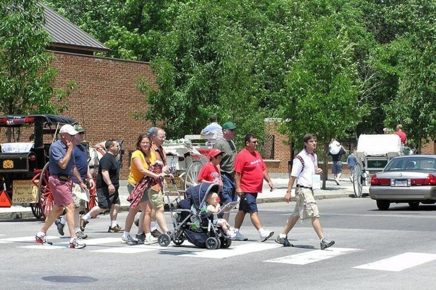 A group of people crossing a street, some with strollers, and a car parked on the side. 2