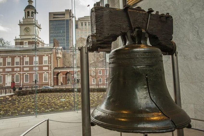 A large bell in an urban setting with a historic building in the background. 5