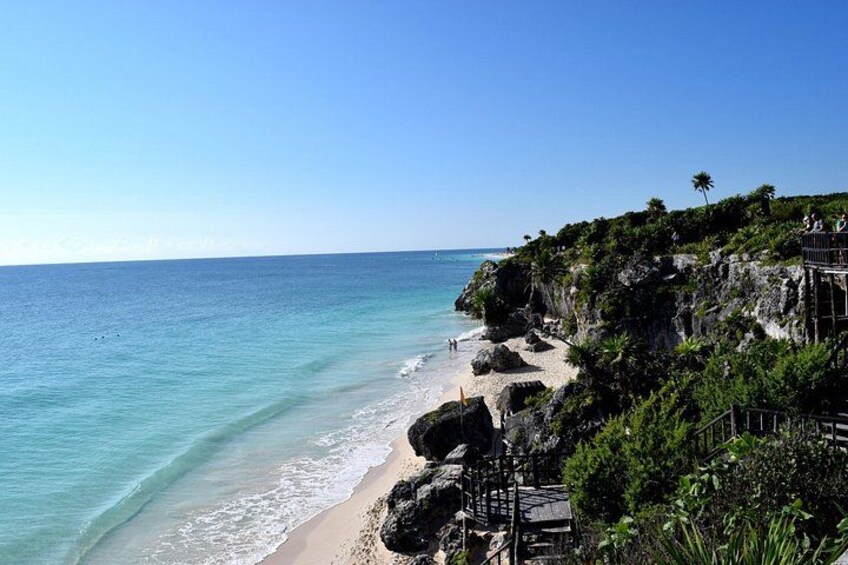 A coastal landscape with a beach, rocky cliffs, and a clear blue sky. 2
