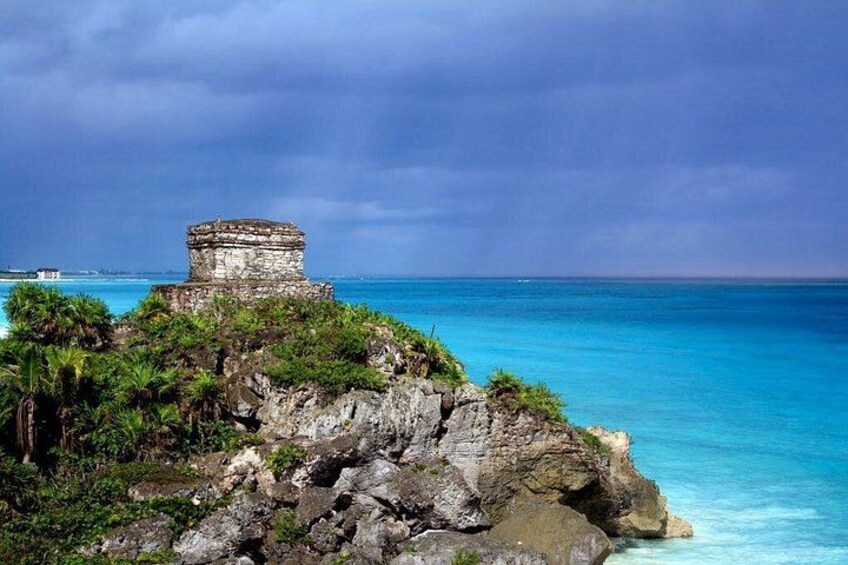 A coastal landscape with a stone structure on a cliff, clear blue sea, and lush greenery. 2