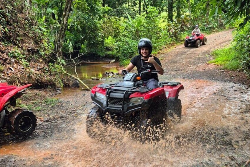 Una persona conduciendo un cuatrimoto por un sendero embarrado en un área boscosa. 2