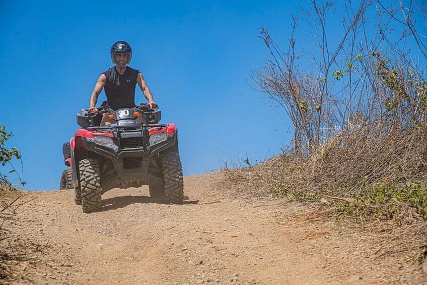 A person riding a red ATV on a dirt path with sparse vegetation. 5