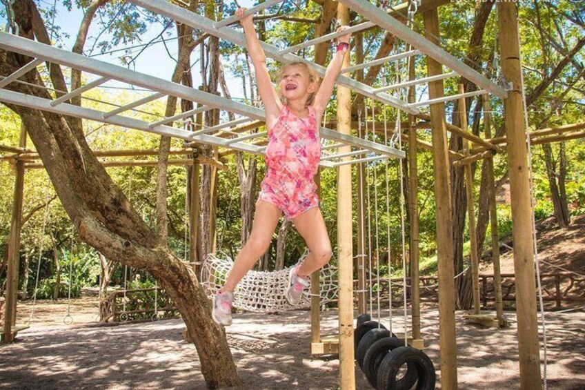 Ein Kind klettert auf einer Seilschwinge in einem Waldspielplatz. 4