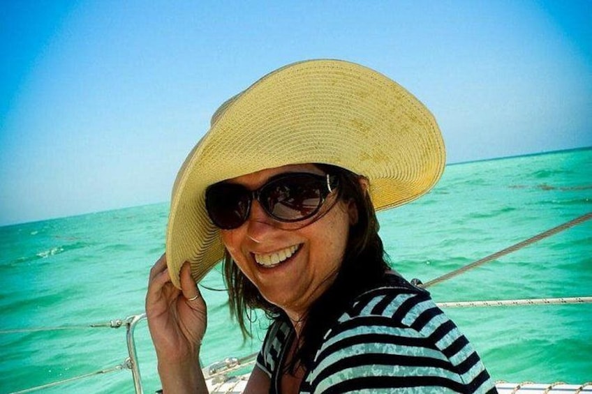 A person wearing a straw hat and a striped shirt, with a clear blue sky and turquoise sea in the background. 1