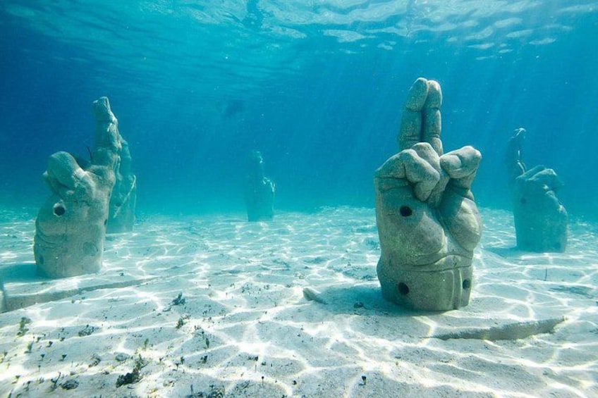 Underwater sculptures resembling hands with fingers raised, set on a sandy seabed. 1