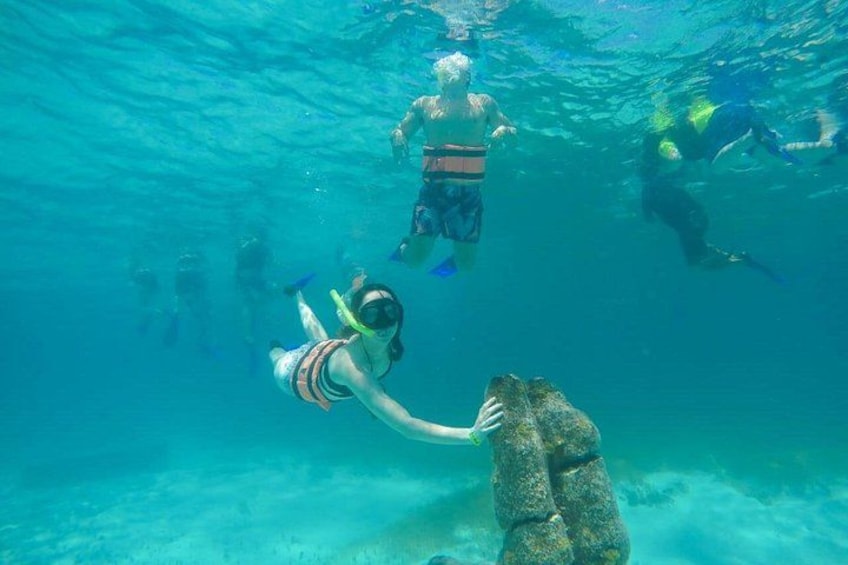 People snorkeling underwater, a large rock formation, and a diver in the foreground. 5