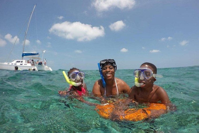 Three people snorkeling in clear blue water with a sailboat in the background. 4