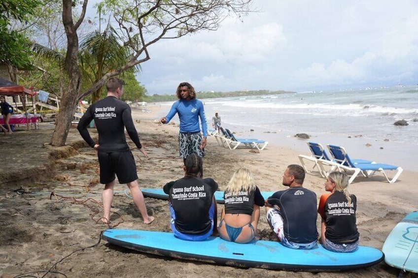 A group of people on a beach with surfboards, some sitting and others standing, under a cloudy sky. 1