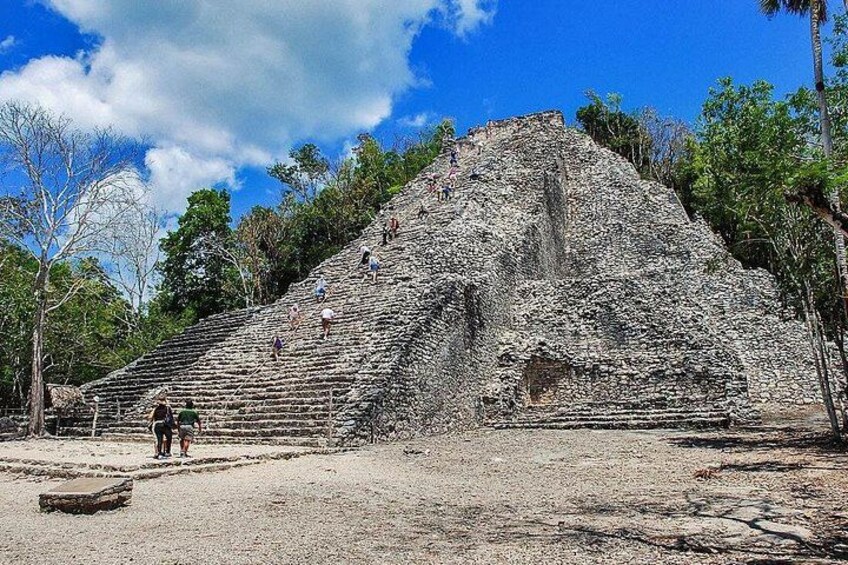 Una gran pirámide de piedra con escalones que conducen a su cima, rodeada de árboles y un cielo despejado. 2