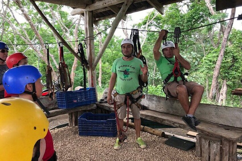People engaged in a zip-lining activity, with trees and a wooden structure in the background. 2